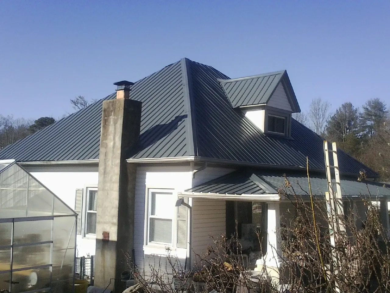 Dark blue standing seam metal roof on a white farmhouse with dormer — Slate & Tile Roof Repair by Roofing Brothers in South Richmond Hill