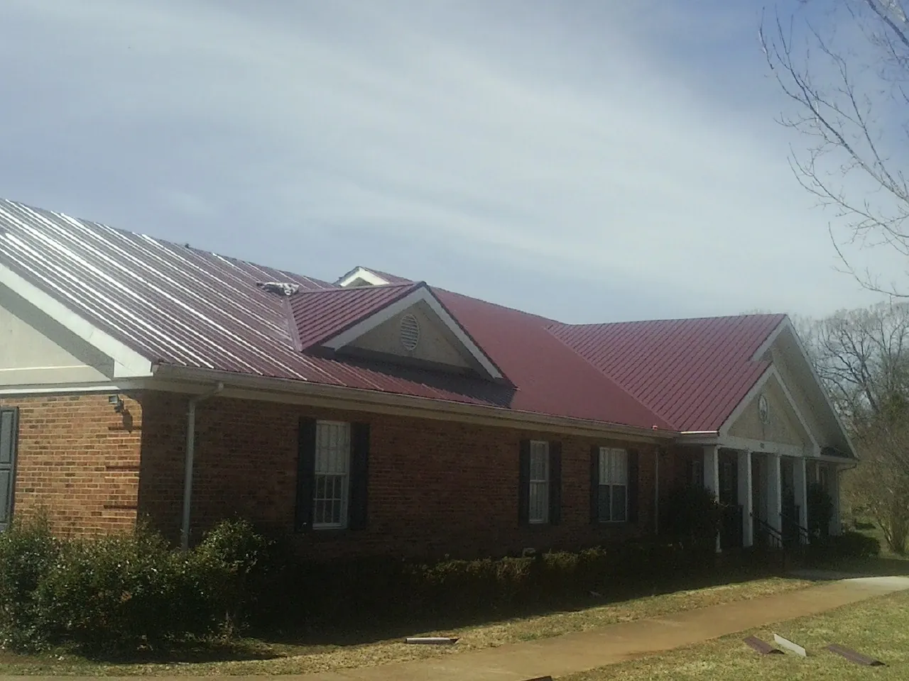 Red metal roof with gabled entries on a long brick building, from a Hail Damage Roof Repair job in South Richmond Hill