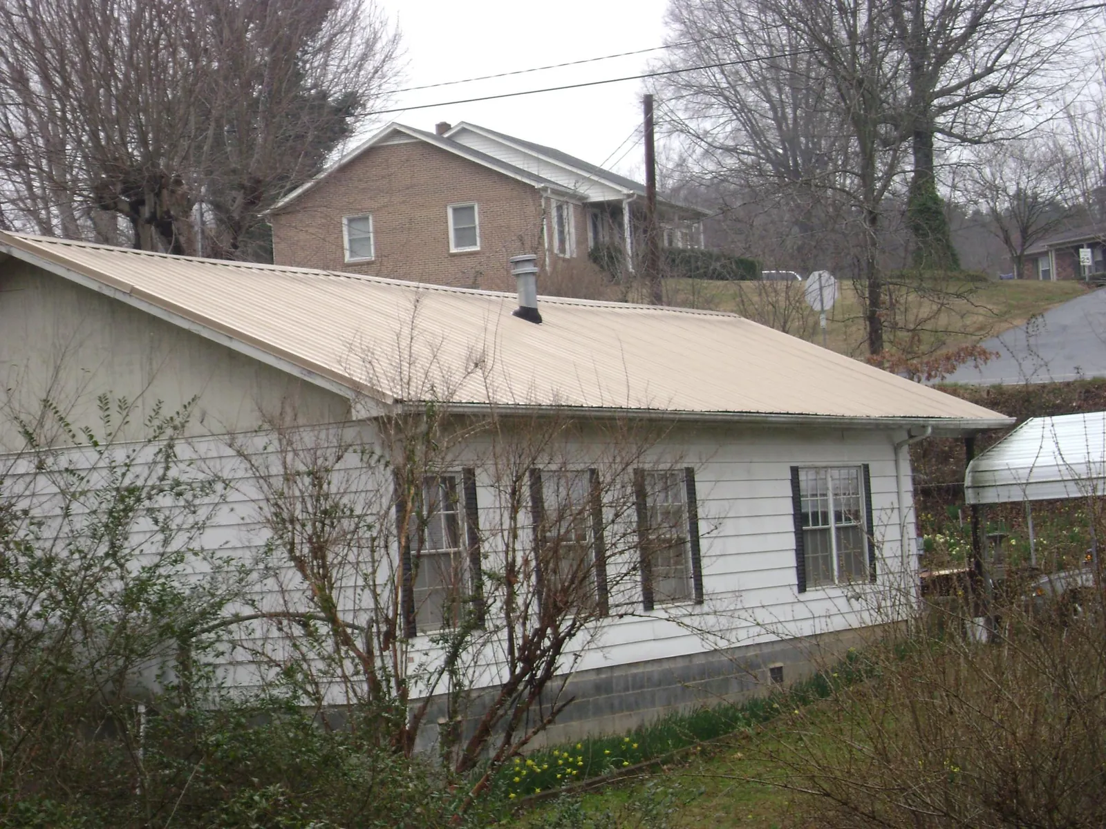 Tan metal roof on a white sided house set into a hillside — Commercial Roofing by Roofing Brothers in South Richmond Hill