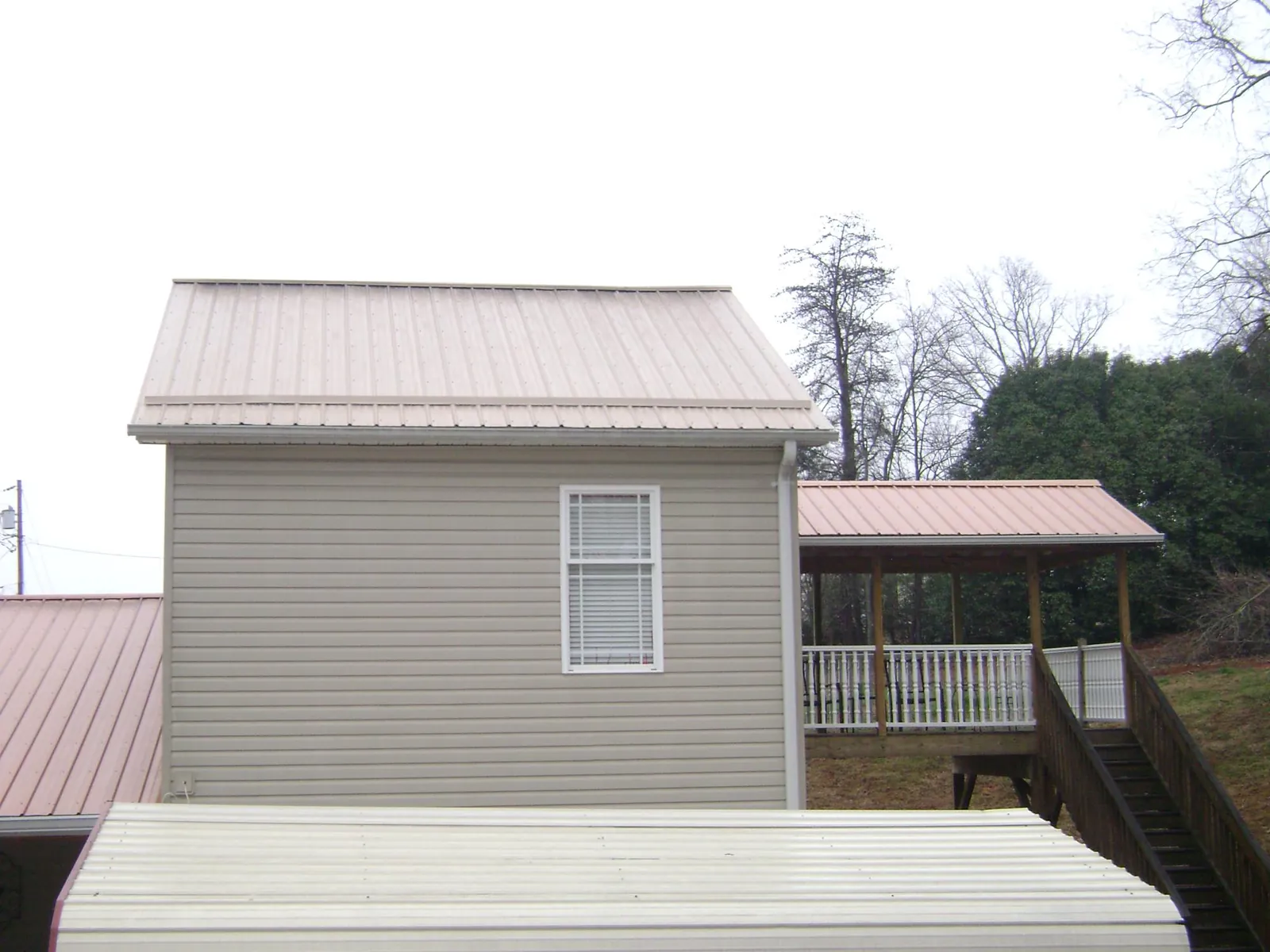Tan metal roofs on a two story addition and attached porch, from a Roof Replacement job in South Richmond Hill